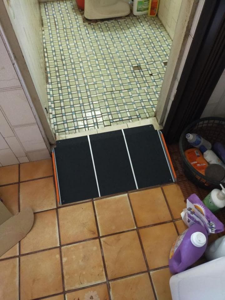 1) 照片顯示了一個帶有橙色邊緣的黑色可伸縮斜坡,放置在浴室地板上的瓷磚上