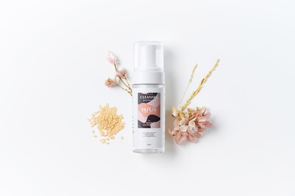 這張「潔面乳」的照片是一瓶白色的潔面乳,旁邊有米粒、花朵和枝葉。