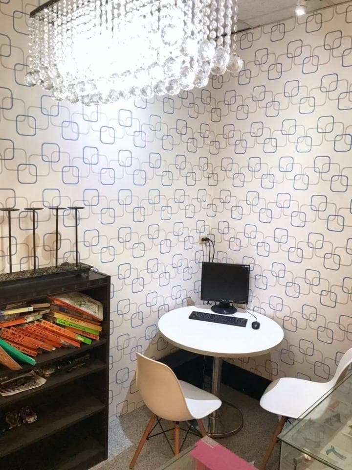 1) 照片顯示一個角落房間,房間裡有一張桌子、兩把椅子、一個電腦螢幕和一個黑色架子,架子上放著書