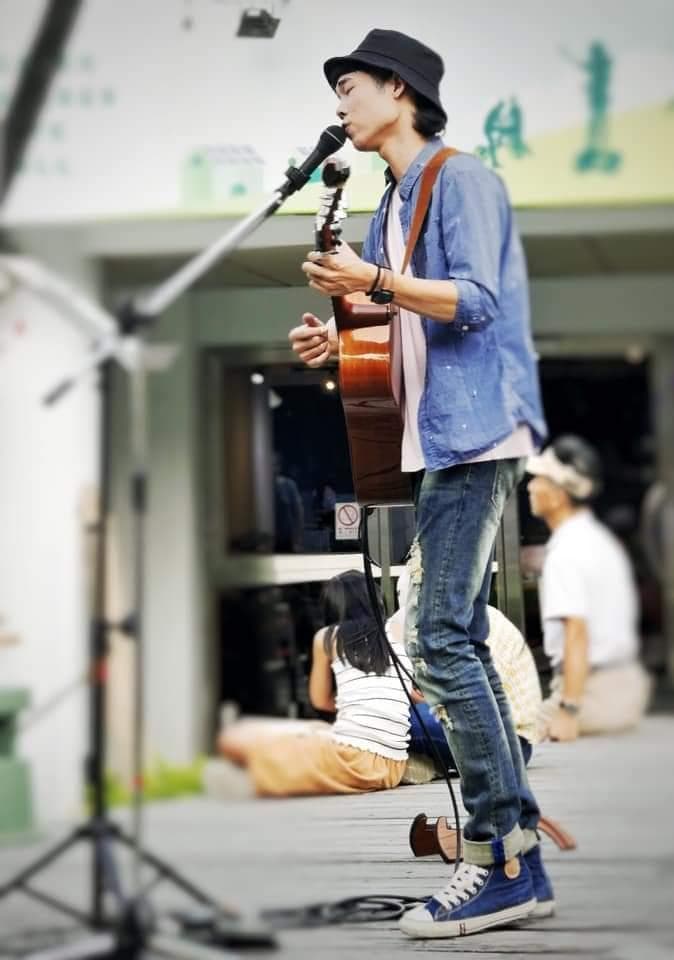 1) 照片中是一位年輕男子穿著藍色襯衫和牛仔褲,戴著黑色帽子,站在街頭表演