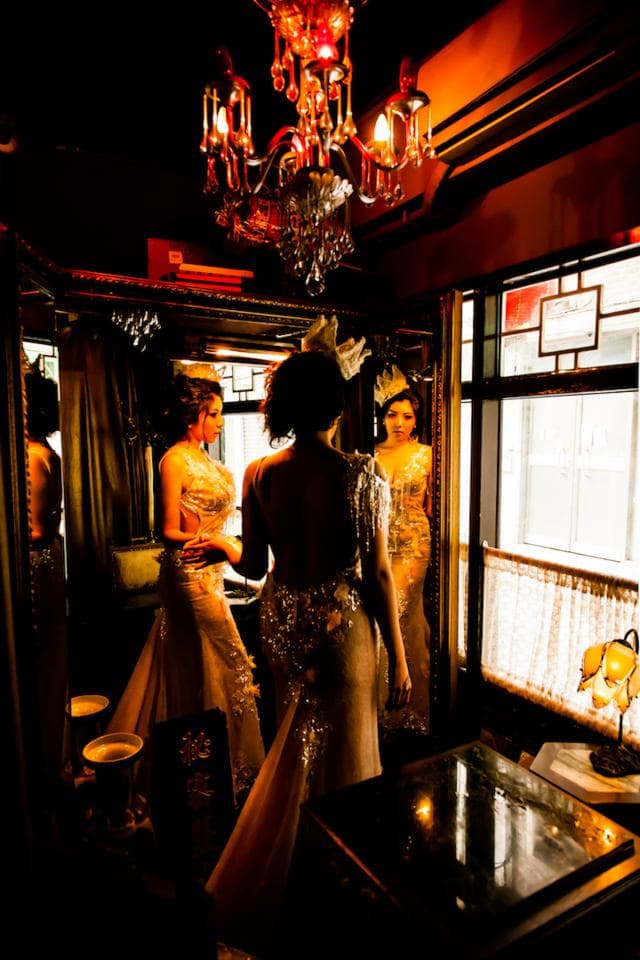 這張「婚紗照」的照片是三個女人在一個房間裡,她們穿著婚紗,其中一個女人站在鏡子前,另外兩個女人站在她後面。房間裡有一個水晶吊燈,燈光很明亮。