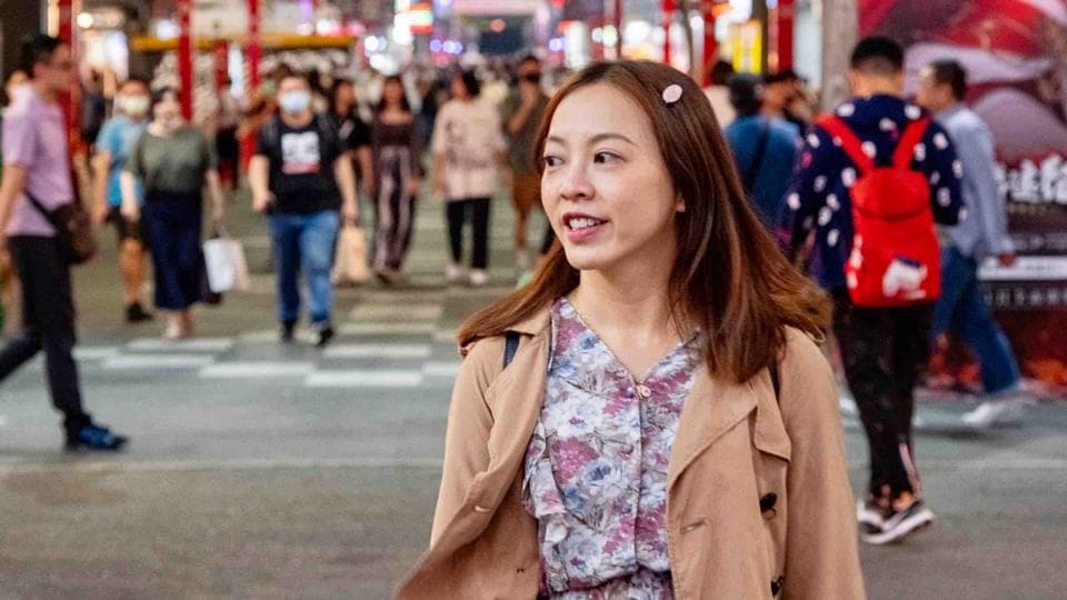 1) 照片顯示一位年輕女性站在繁華街道上,穿著棕色外套和花卉洋裝,背景有許多行人