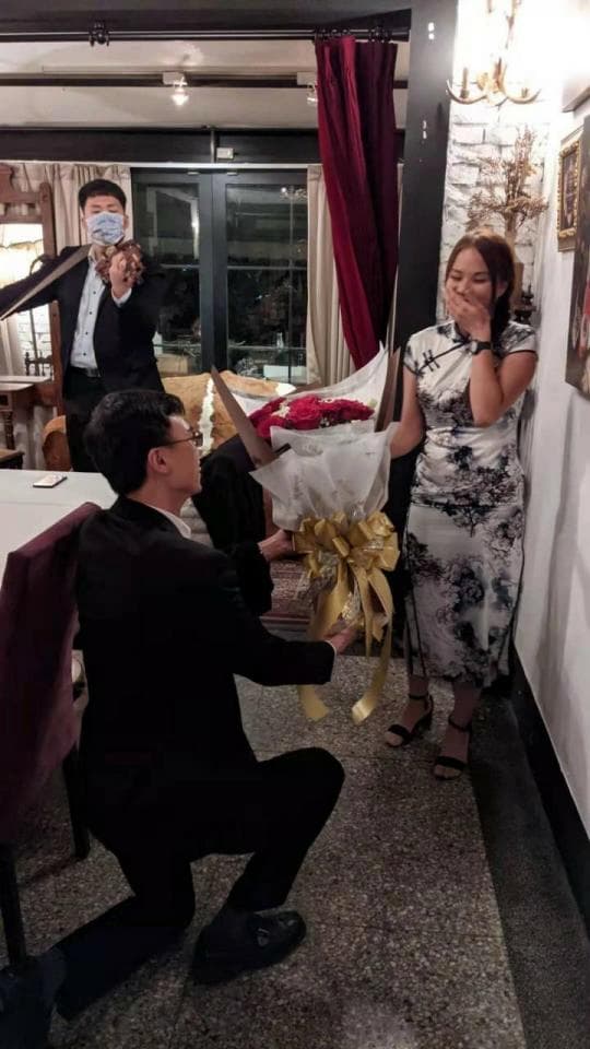 這張照片是 一個男人正在向一個女人求婚,他跪在地上,手裡捧著鮮花。