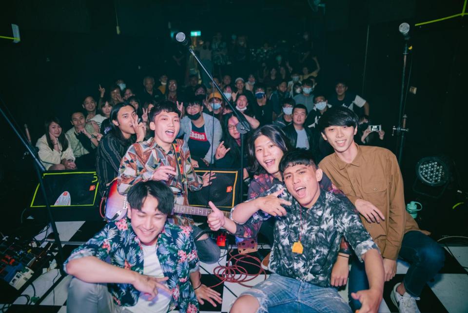 這張照片是一群年輕人在一個昏暗的室內場地演奏音樂。照片中最主要的是一個樂團,他們正表演著,其中一位吉他手正彈奏著紅色電吉他。