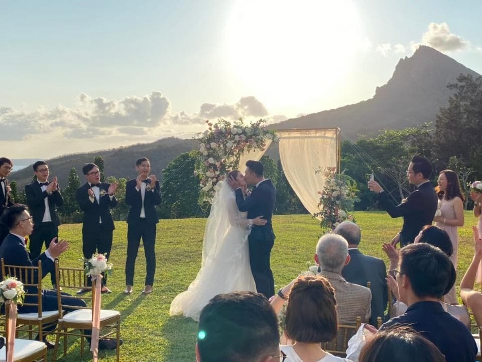 這張照片是一對新人正在交換誓言,他們在一個美麗的戶外場地舉行婚禮,背景是山景和藍天,周圍是親朋好友。