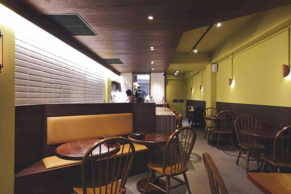 這張照片是餐廳裡的一角,有一個舒適的長沙發座位,前面擺放著木質桌椅。桌子上的燈光和壁燈的溫暖光線營造出溫馨的氛圍。