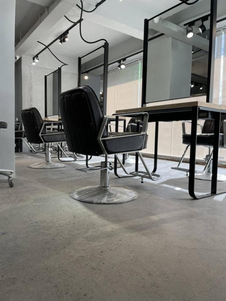 這張「美髮沙龍」的照片是四張黑色的椅子,以及一面大鏡子。椅子有輪子,可以方便移動。鏡子很大,可以讓顧客清楚地看到自己。地板是水泥,看起來很乾淨。