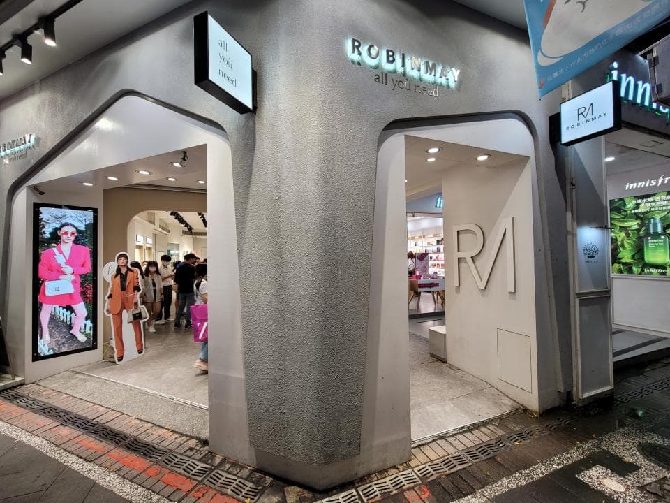 這張「服飾店」的照片是一個現代化的商店,店門口有「ROBINMAY」的招牌,店裡有幾個顧客在選購商品。