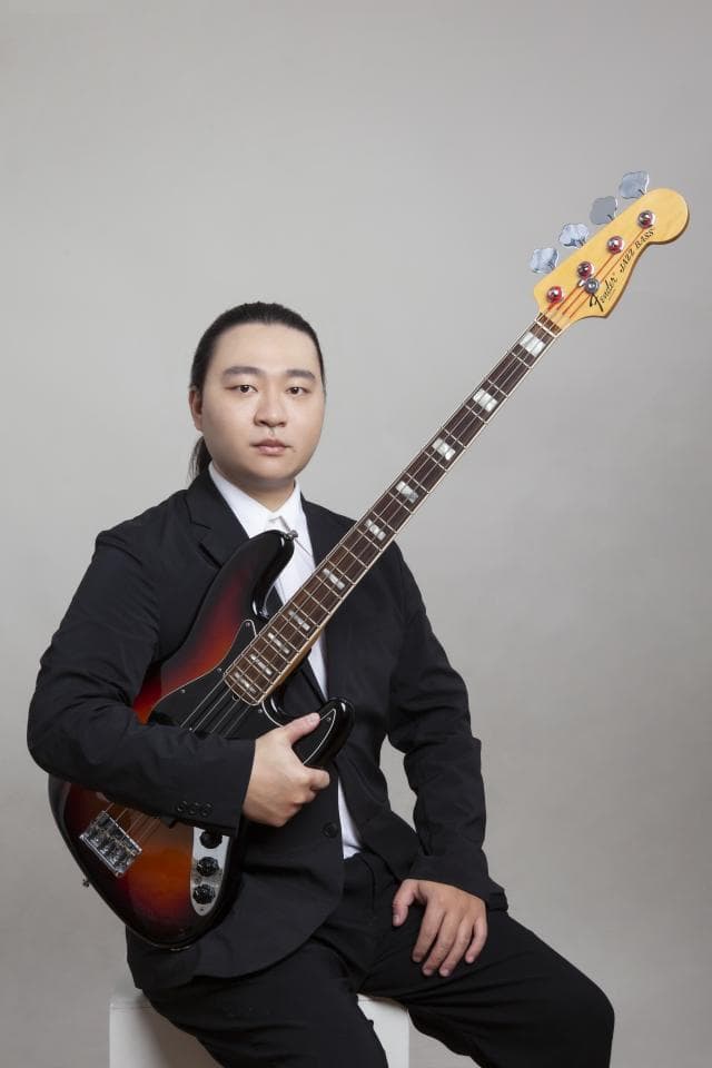 這張照片是一個穿著西裝的年輕男子,他正在彈奏一把貝斯。
