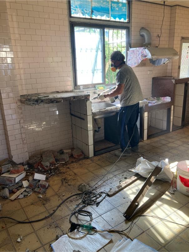 1) 照片顯示一個工人正在拆除廚房的流理台,地上有許多瓦礫和工具