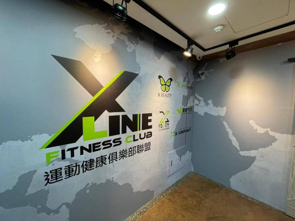 這張照片是健身房的牆壁上印著「X-LINE FITNESS CLUB 運動健身俱樂部」的標誌。