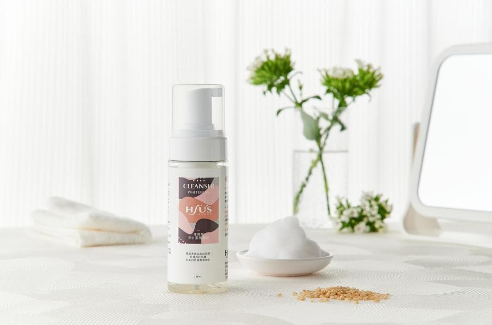 這張「洗面乳」的照片是,展示了洗面乳的瓶子,以及一旁的花瓶、毛巾和鏡子,畫面呈現乾淨整潔的氛圍。