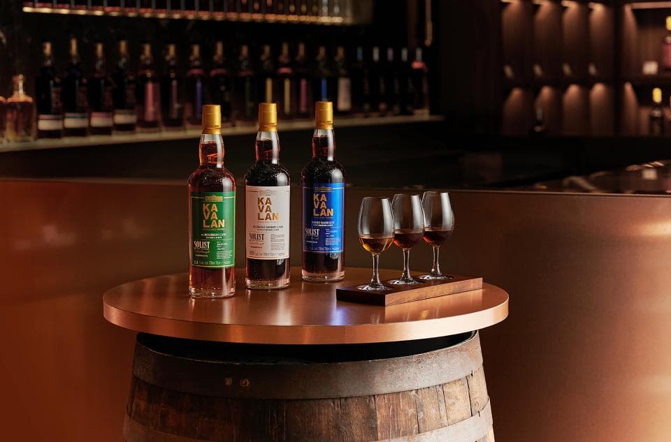 這張「酒類陳列」的照片是三瓶不同顏色的酒和三個高腳杯,放在一個銅色的圓形木桶桌上。