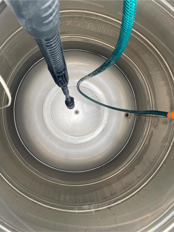 1) 照片顯示一個金屬容器的內部,容器內部有一個黑管從頂部伸入,容器內部有一條綠色的軟管,從容器邊緣延伸至中心,在容器的底部,可以看見一個金屬蓋