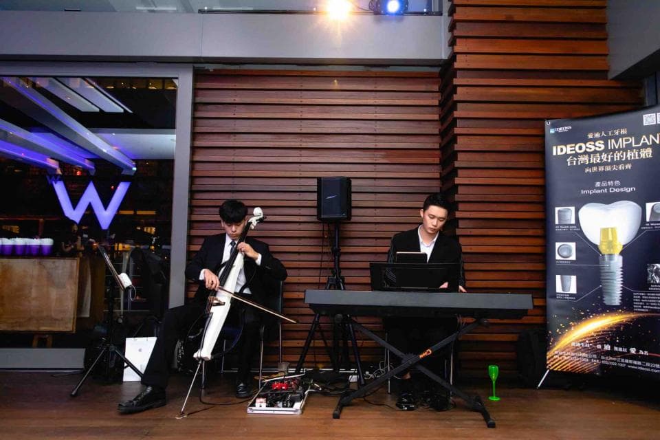 這張照片是一個音樂演奏的場景,照片中的人物正在演奏大提琴,背景是一間現代化的飯店大廳。