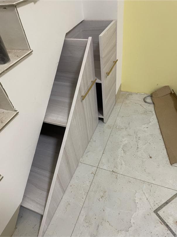 這張照片是一個利用樓梯空間建造的儲物櫃。櫃子是木紋色的,並且帶有金色的把手,看起來很時尚。