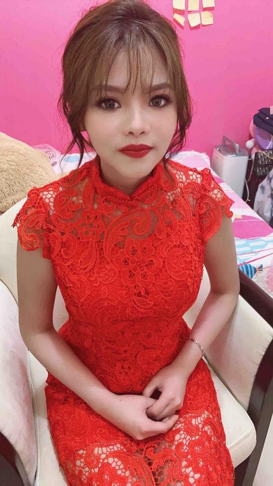 這張照片是一個穿著紅色蕾絲旗袍的年輕女子,她坐在一張白色椅子上,背景是粉紅色的牆壁。