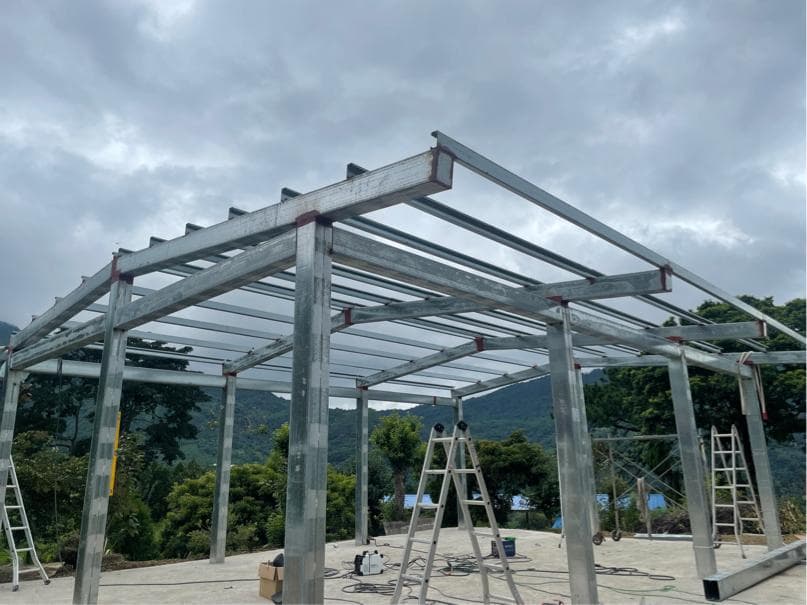 1) 照片顯示一個鋼鐵結構的建築,其樑柱清晰可見,屋頂尚未完成,周圍環繞著樹木和綠地