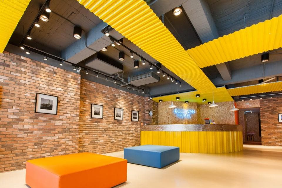 這張「酒店大廳」的照片是一個現代化的酒店,有著明亮的黃色天花板和紅磚牆。照片中可以看見酒店的前臺和一些休息的座椅。