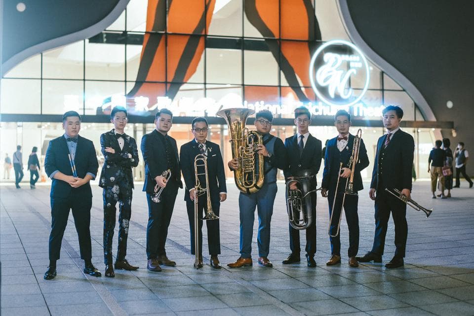 1) 照片中,七位身穿西裝的男士站在建築物前,手持各式的樂器,似乎是在準備演奏