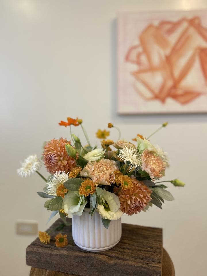 1) 照片中有一束橙色、白色和黃色的花卉,放在一個白色花盆裡