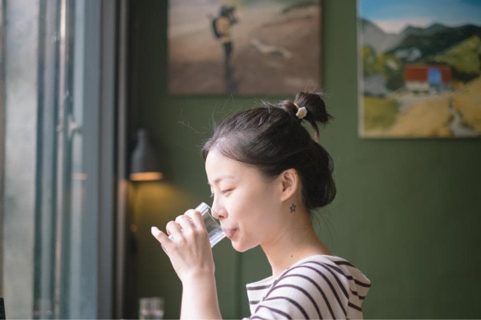 這張照片是一名女性在窗邊喝水,她專注地注視著水杯,享受著喝水的時光。