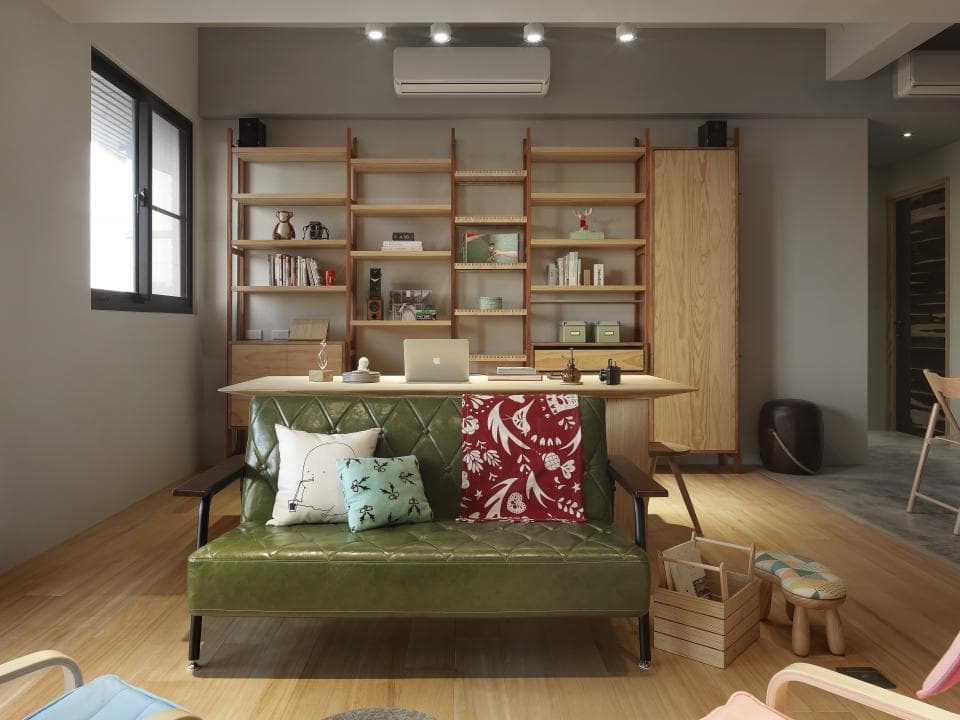 這張照片是一個時尚的書房,中間擺放了一張綠色的沙發,沙發上有兩個抱枕,一個是白色的,另一個是藍色的,沙發前方是木製的桌子,桌子上放著一個筆記型電腦。