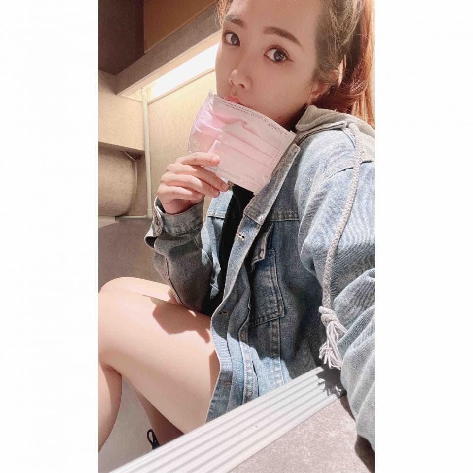 這張照片是一個女生戴著粉色口罩,穿著牛仔外套,坐在戶外階梯上。