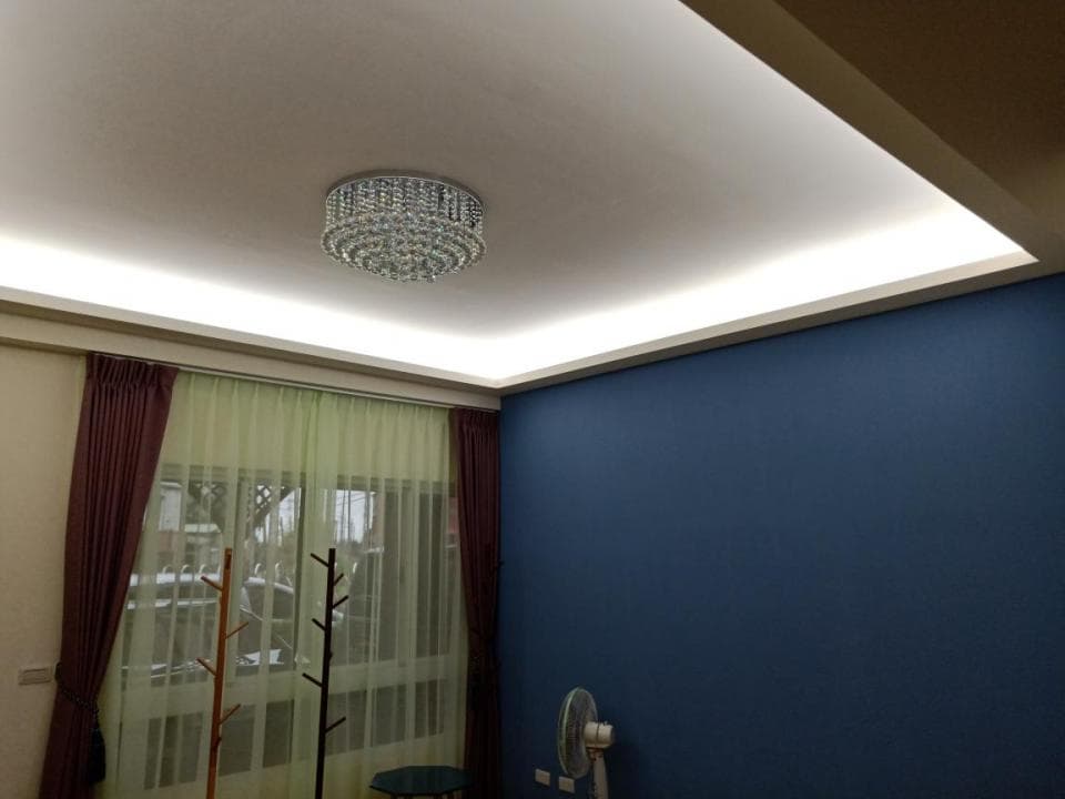 1) 照片顯示一個客廳,牆壁塗成藍色,裝飾著一個水晶吊燈,落地窗裝有窗簾,靠近窗戶處放著一個置物架,牆壁上還有裝飾的線燈