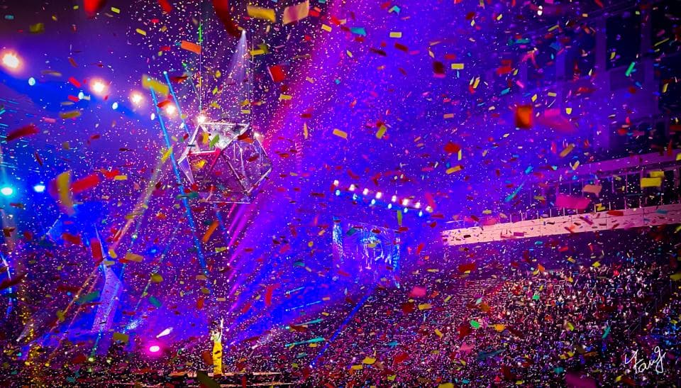 這張照片是一場音樂會,舞臺上有一個巨大的玻璃球,觀眾們正從空中拋下五顏六色的彩帶,場面十分熱鬧。