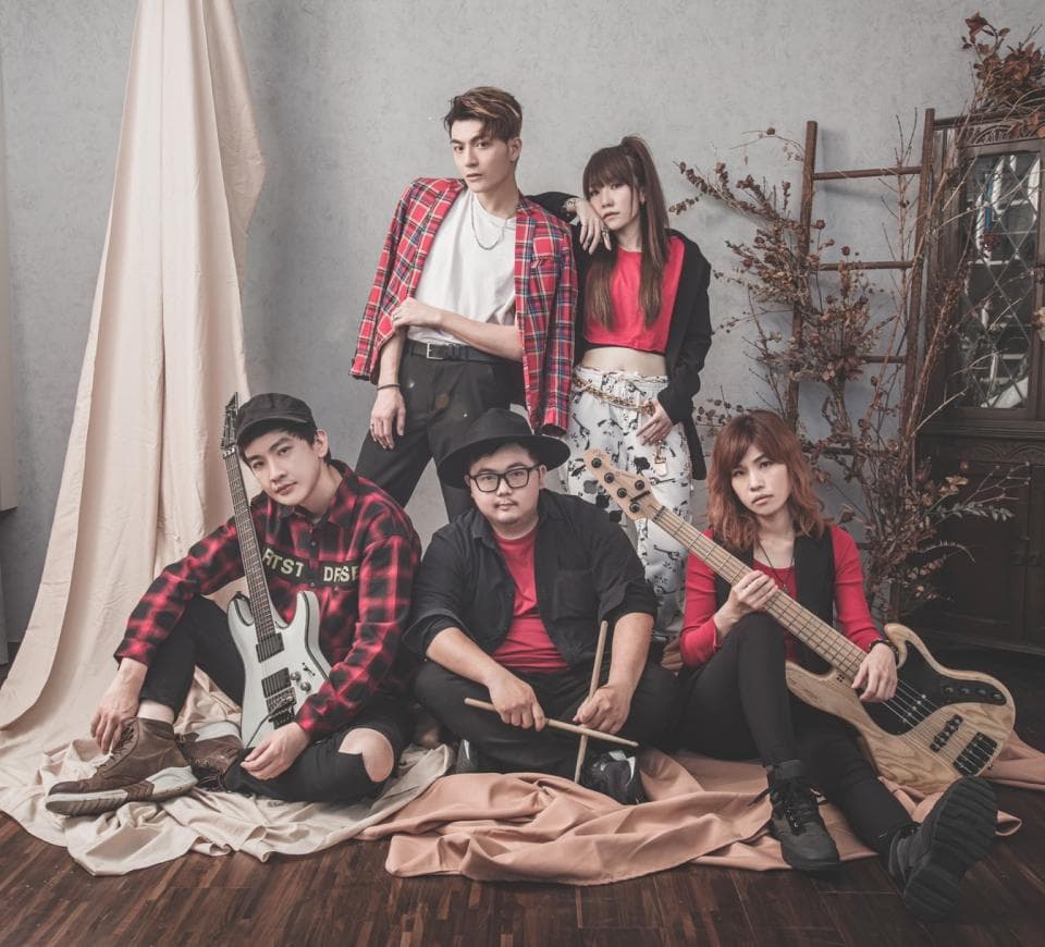 這張照片是五個朋友在一個工作室裡拍照,他們正擺著姿勢,看起來很享受拍照的過程。他們都穿著很時尚的衣服,其中一位女生穿著紅色的上衣和黑色的褲子,另一個女生穿著淺色的上衣和黑色的褲子,而三位男生穿著紅色的格子襯衫,看起來很酷。他們顯然是互相認識的,而且關係很好。