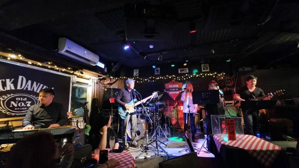 這張照片是一家酒吧裡,四個樂手正在表演。樂團裡有一位吉他手、一位鍵盤手、一位鼓手和一位貝斯手。他們正在為臺下的觀眾表演。