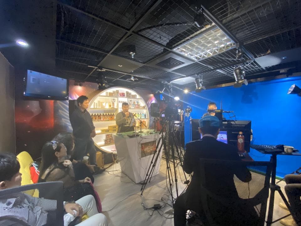 這張「直播現場」的照片是一群人在錄製節目,背景是一面藍色的牆,前方有兩個攝像機,其中一個對準了主持人,另一個對準了觀眾。