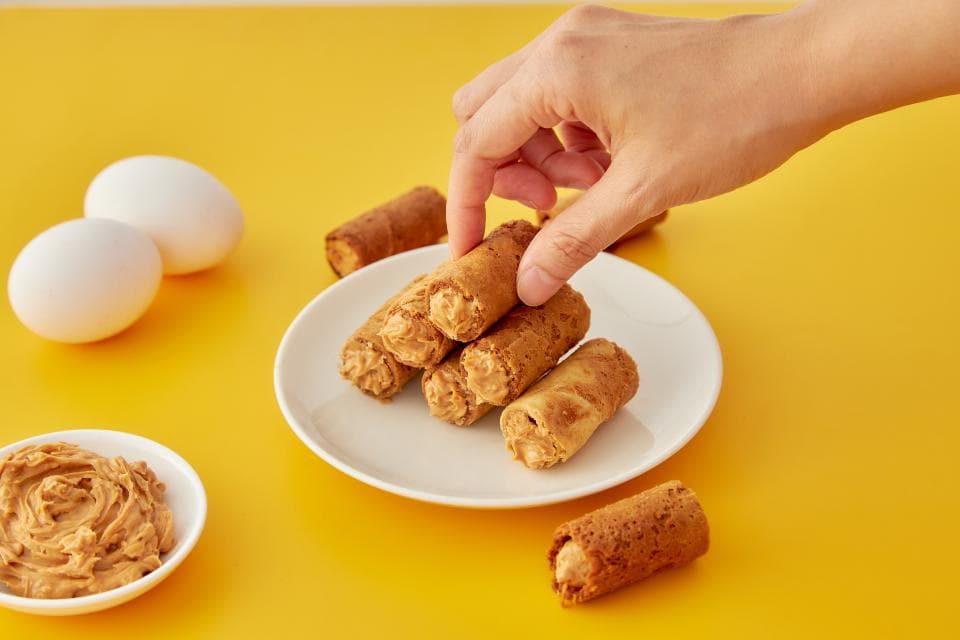 這張「蛋捲」的照片是一些蛋捲放在白色盤子裡,旁邊還有一碟花生醬和兩個雞蛋。