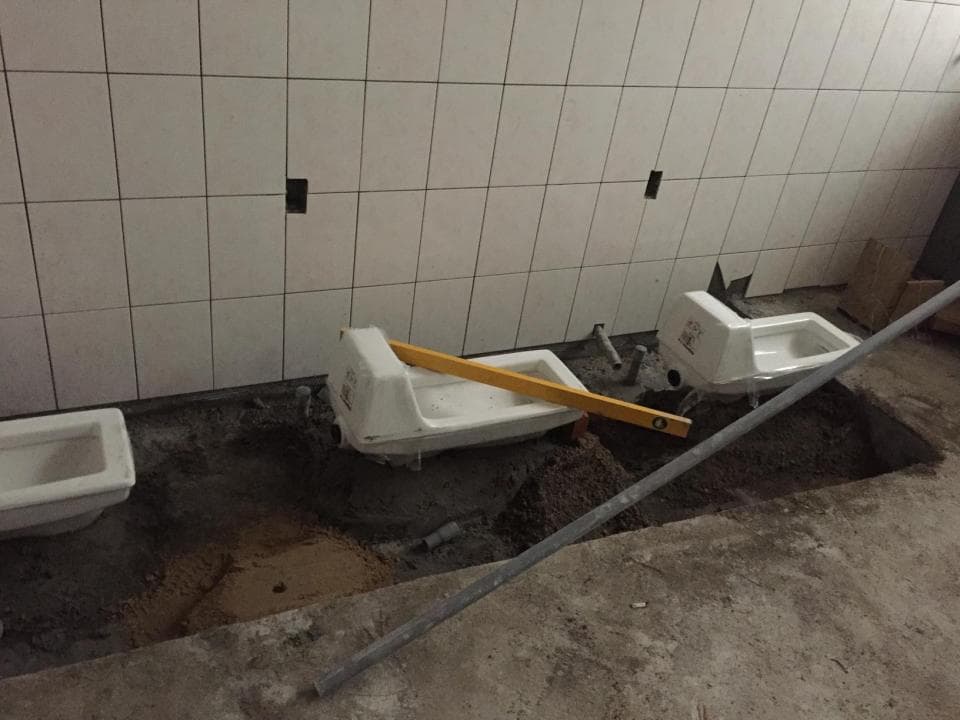 這張照片是一個正在建造的廁所。照片中有一個安裝好的馬桶,以及一個正在安裝的馬桶。馬桶周圍的地板還沒有鋪設好,可以看到水泥和一些工具。