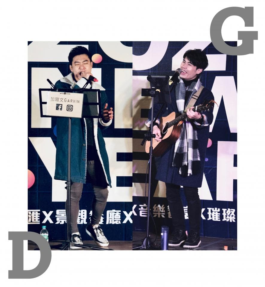 這張「兩位歌手在臺上表演」的照片是,一位歌手穿著藍色外套,拿著麥克風唱歌,另一位歌手穿著黑色外套,拿著吉他唱歌。