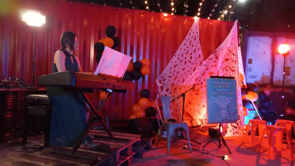 這張「音樂會」的照片是一個女人在鋼琴上演奏,背景是紅色牆壁和白色裝飾,還有舞臺燈光和音響設備。