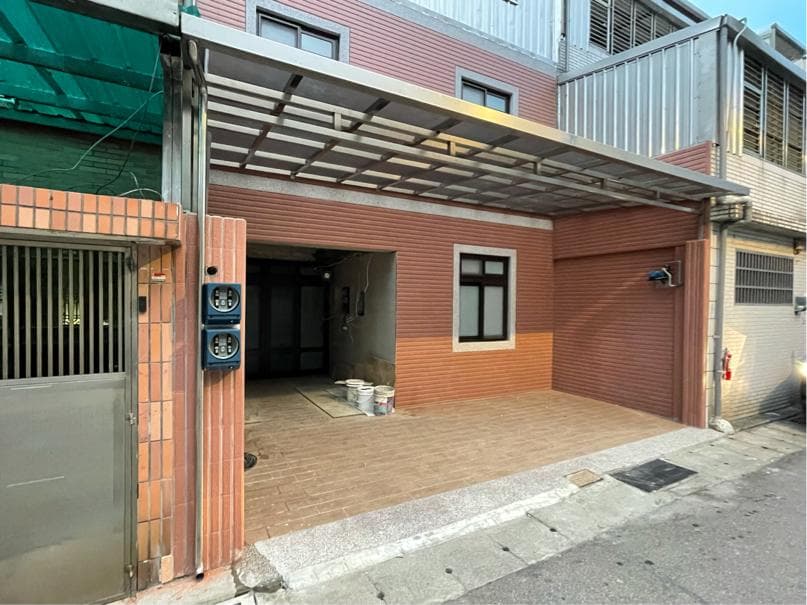 1) 照片顯示一棟兩層樓的住宅,前方有水泥遮雨棚,門前鋪著紅棕色地磚,地上有兩個白色水桶