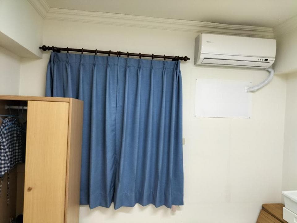 1) 照片顯示一個房間的一角,房間有一扇窗戶,窗戶上裝著藍色的窗簾,房間裡還有衣櫃和一個冷氣