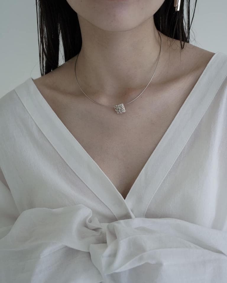 1) 照片顯示一個穿著白色襯衫的女性,戴著一條細金鍊,鏈子上有一個小巧的立體方形墜飾