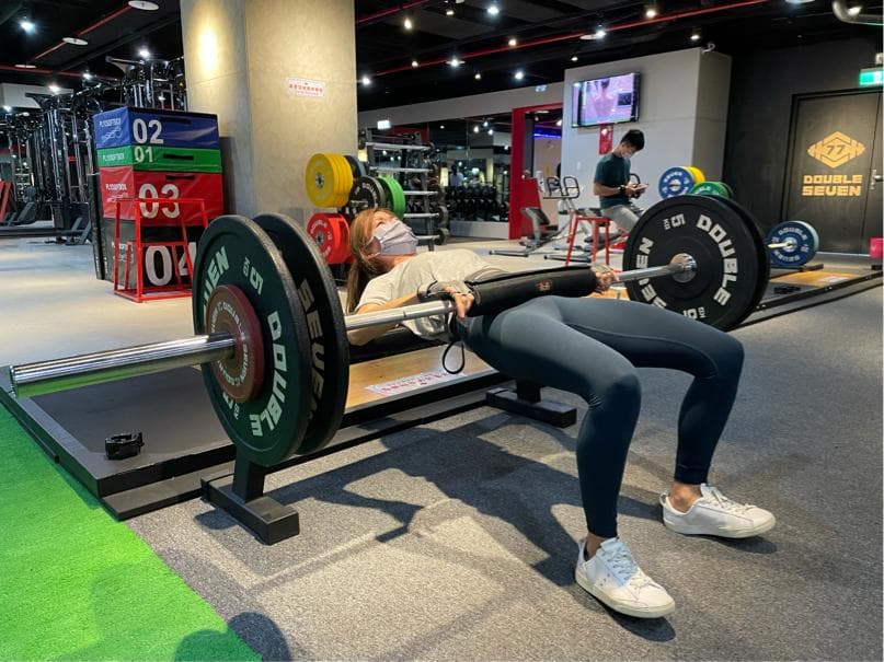 這張照片是一個女生在健身房做舉重訓練。她正在用槓鈴做深蹲,這是一個鍛煉腿部和臀部的很好方法。她看起來很努力,很專注。