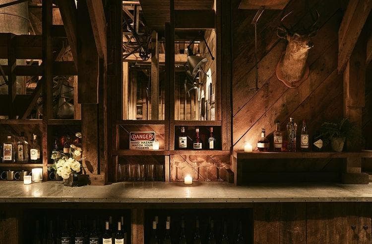 這張酒吧的照片是一個木製的酒吧,上面放著酒瓶、杯子以及蠟燭,牆上掛著一個動物頭。