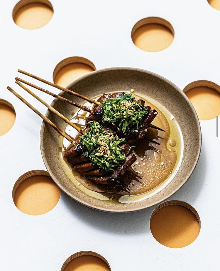 這張「烤肉串」的照片是兩串肉串,上面放著香草和芝麻,放在一個淺色的碗裡。