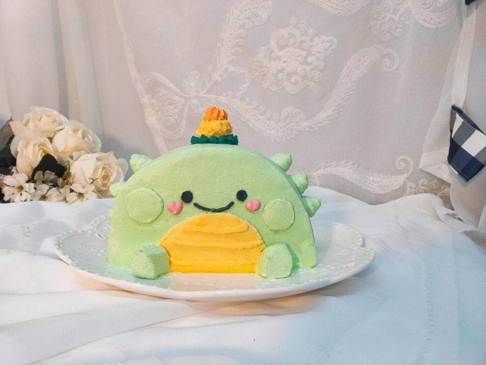 這張照片是一隻可愛的綠色恐龍蛋糕,它有一個黃色的肚子和一個可愛的微笑。 它的頭上還有一頂小帽子。