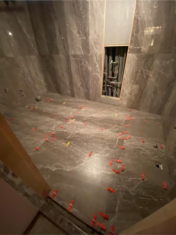 1) 照片顯示一個正在裝修的浴室,地板鋪設了灰色大理石,地板上還有紅色的塑膠墊片