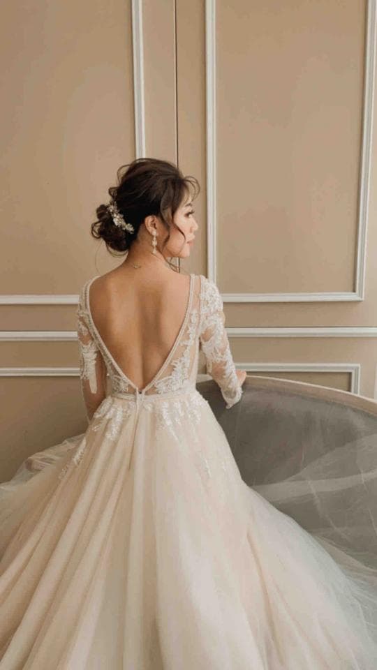 這張「新娘婚紗」的照片是一個穿著白色蕾絲婚紗的女性,她站在一個房間裡,背景是一面牆。她正在轉身,展現出婚紗的背部設計,蕾絲花紋非常細緻。
