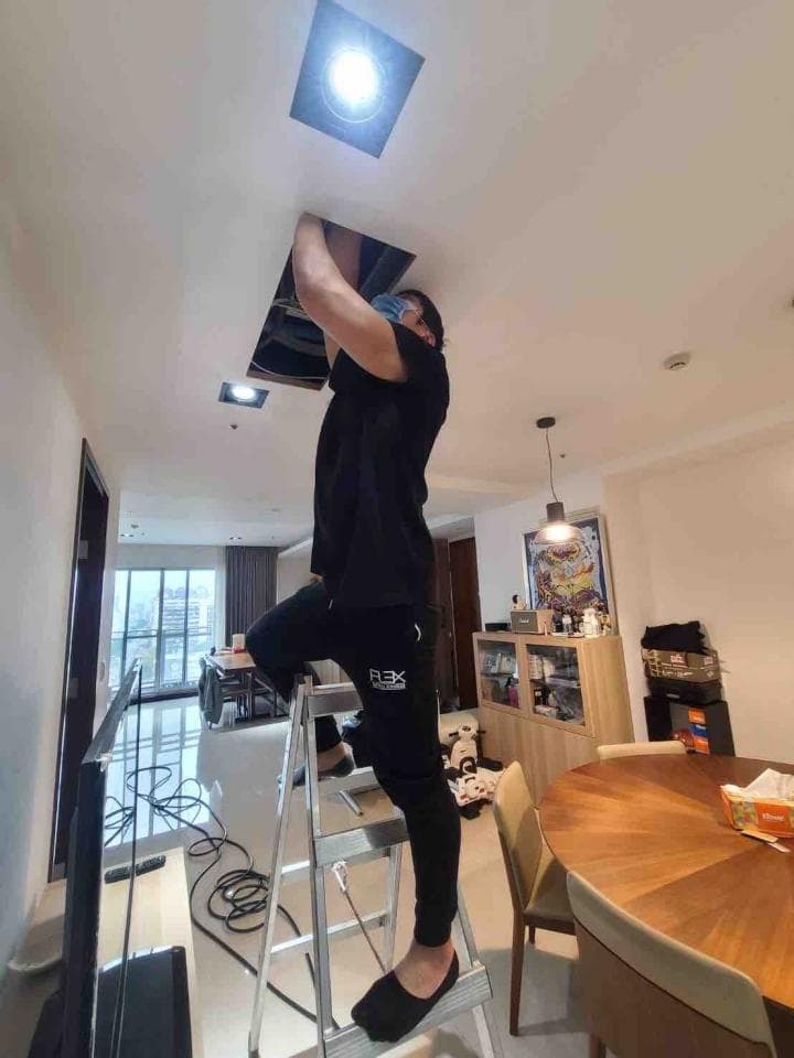 1) 照片顯示一位穿著黑色上衣和褲子的男子正在安裝天花板燈,他站在梯子上,並用手扶著天花板