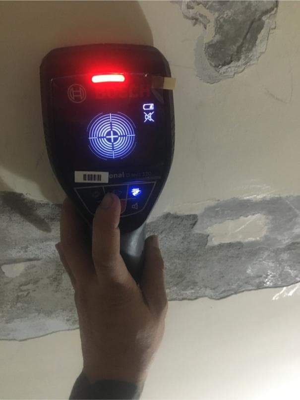 這張照片是一個牆壁上的探測器,它正在檢查牆壁上的裂縫。探測器上有紅色的指示燈和藍色的顯示屏,顯示出牆壁的結構。