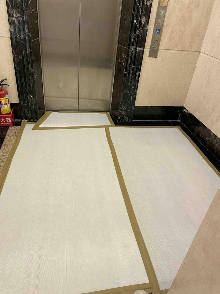 1) 照片顯示一個電梯門和地板上兩個帶有金邊的白色方形地毯