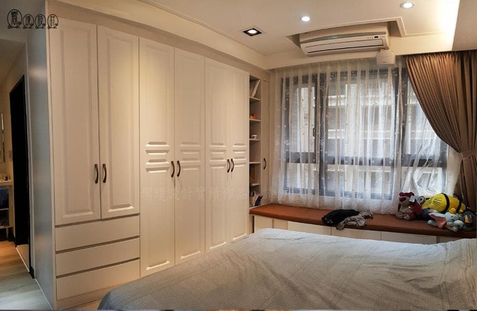 這張照片是一間臥室,最主要的部分是一個大型的白色衣櫃,它佔據了房間的一大半,衣櫃的設計非常簡潔,而且表面是光滑的白色,看起來非常乾淨整潔。衣櫃的門上還裝有黑色把手,增添了一些時尚感。